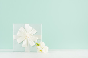 Beautiful fresh spring festive background with elegant standing gift box, white flowers freesia in green mint menthe interior on white wood board.