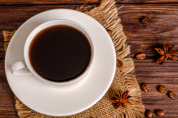 Cup of black aromatic coffee in a white cup with anise stars and cinnamon sticks on a wooden background.