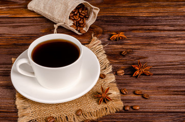 Cup of black aromatic coffee in a white cup with anise stars and cinnamon sticks on a wooden background.