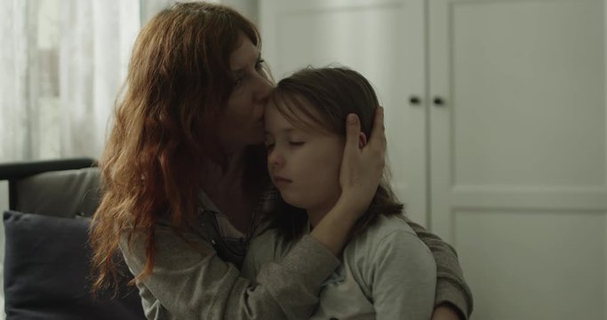 Mama przytula chorą c&oacute;rkę i całuje ją w czoło.