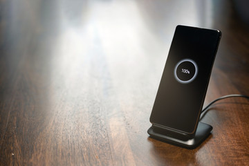 smartphone wireless charging on charging stand with 100 percent icon on screen on wooden table