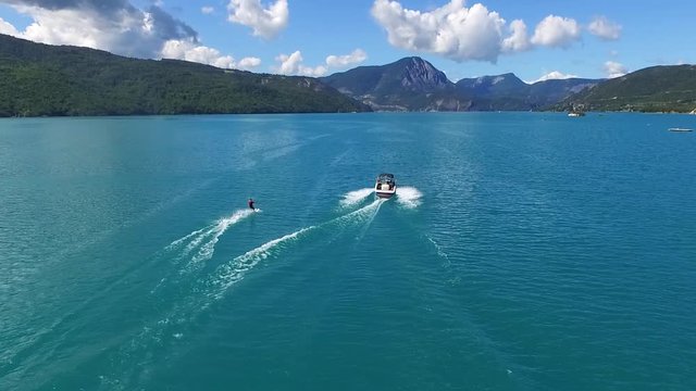 Water skiing on lake aerial view. Riding water board ski behind motorboat.