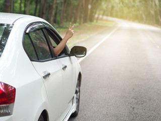 asian woman show her hand out from the window car and show peace sign during road trip on the road. use for travel concept.