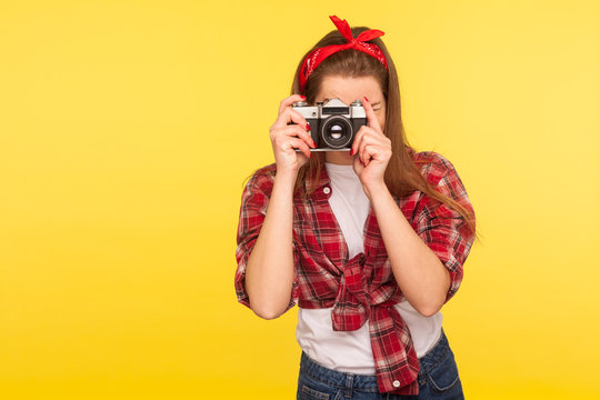 Portrait of pinup girl in checkered shirt and headband taking picture with old fashioned camera, traveler making photo