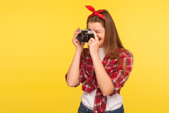 Portrait of happy pinup girl in checkered shirt and headband taking picture with old retro camera and smiling
