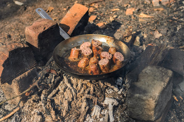 Grilled sausages are fried in a pan over a fire in a forest on a picnic