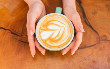 Beautiful pattern heart created by microfoam. Coffee shop and cafe concept. Female hands cappuccino. Design on surface of latte. Challenge for latte artist. Top view coffee cup on wooden table