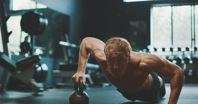 Strong muscular man working out in the gym doing kettlebell push ups in slow motion, determined man pushing his physical limits in the gym
