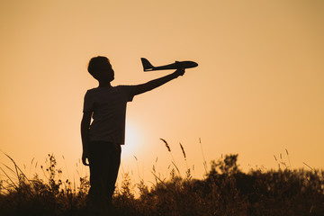 Black silhouette of young caucasian kid isolated on sunny golden sunset sky background. Boy playing...