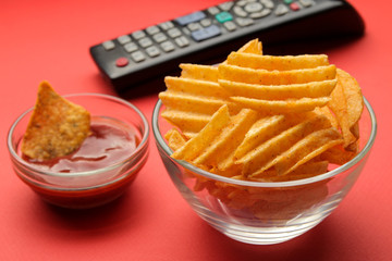 Chips and tv remote control on a bright red background. Concept of watching a movie or video at home.