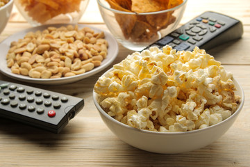 Popcorn, various snacks and tv remote on a natural wooden table. Concept of watching a movie or video at home.