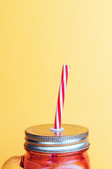 Top of a glass jar with a tin lid and a red and white straw with a cold drink.
