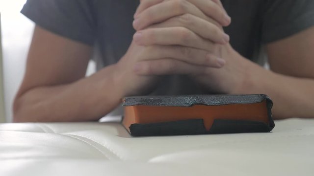 man praying indoors at bedtime on bible. religion concept evening prayer human brunette hands lifestyle on bible praying by bed