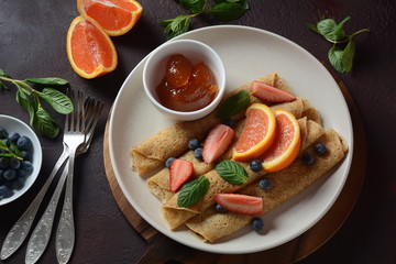 Sweet pancakes wrapped with fresh mint, strawberries, blueberries, oranges and jam. Healthy breakfast concept
