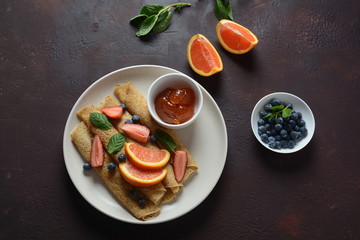 Sweet pancakes wrapped with fresh mint, strawberries, blueberries, oranges and jam. Healthy breakfast concept