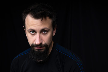 a close up portrait of a young man with beard in dark clothes on a dark background