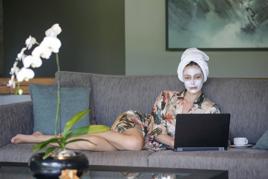 Young Woman Sitting At Home With Face Beauty Mask In Front Of Her Laptop. Cozy Time At Home. Self Time And Home Spa Concept. Coronavirus Outbreak And Self-quarantining Concept.