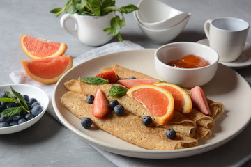 Sweet pancakes wrapped with fresh mint, strawberries, blueberries, oranges and jam. Healthy breakfast concept
