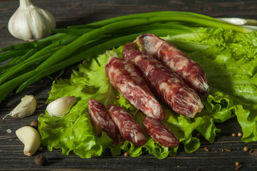 Sausage with garlic and herbs. On the brown table is a sausage with greens. Delicious country food. Delicious sausage with herbs and garlic.