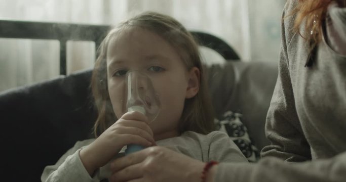 Mama podaje chorej c&oacute;rce nebulizator i całuje ją.