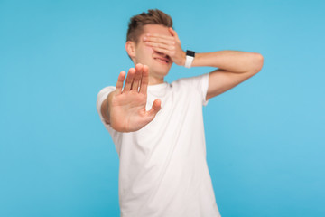 I'm not watching! Portrait of scared shamed man in casual white t-shirt covering eyes and showing...