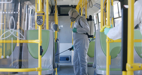 HazMat team in protective suits decontaminating public transport, bus interior during virus outbreak