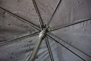 Wet textured surface of a black umbrella with drops of water after rain