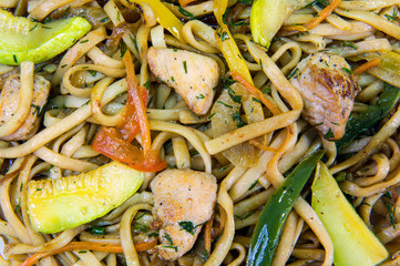 Fried noodles in vegetable oil with colored peppers and cucumbers, as well as pieces of pork
