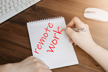 Top view, a woman's hand writing the word "Remote work" in a Notepad . Coffee Cup on the office Desk
