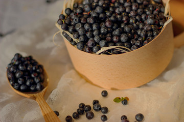 Blueberries in a wooden box, next to a wooden spoon with berries, lie on a white canvas, still life with wood bowl with berries
