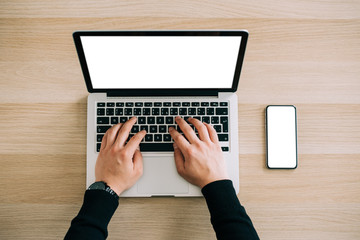 Man's hands using laptop with blank screen on desk in home interior. Mockup image white screen.