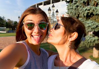 Mother and adult daughter are doing selfie in the park going crazy and showing tongueSunset light.Happy and positive emotions.Hipster family.Parents and teenagers.Summer vacation self-portrait