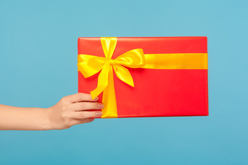 Closeup of woman arm holding red gift box with yellow ribbon, romantic surprise for Valentine's day, nice present for Christmas holidays, anniversary or birthday. indoor studio shot, blue background