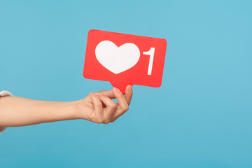 Appreciate content with heart button. Closeup of hand holding like icon of social media, emoji sign to follow subscribe interesting blog, popular forum. indoor studio shot isolated on blue background