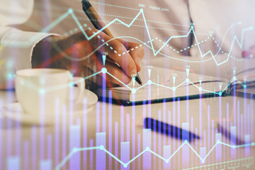 Double exposure of man's hands writing notes of stock market with forex chart.