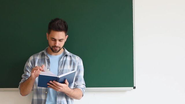 Male student reading book near blackboard in classrom