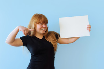 young woman of Caucasian appearance with red hair holds a poster with copyspace with two hands, she...