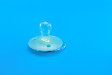 light blue baby pacifier lies on a blue background, object baby accessories with a copy space.