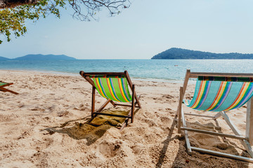 Sun lounges on sand of tropical island beach. Some deck chair for relaxing tourists near an ocean