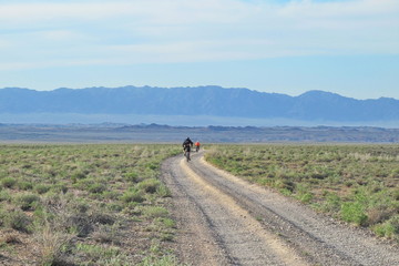 cyclists ride towards the mountains on the steppe road, Kazakhstan.
