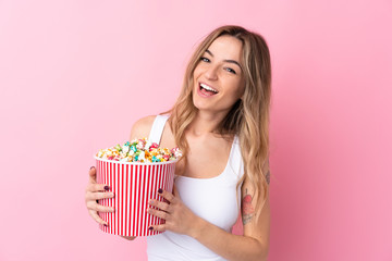 Young woman over isolated pink background holding a big bucket of popcorns