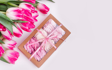 A box of sweets and a bouquet of flowers on a white background. Homemade marshmallows and tulips