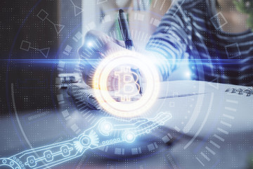 Cryptocurrency hologram, bitcoin, ico theme over hands taking notes background. Concept of...