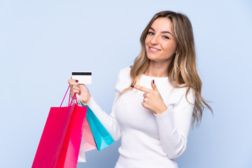 Young woman over isolated blue background holding shopping bags and a credit card