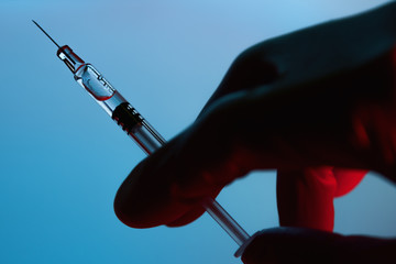 Hand holds syringe on blue background, Covid-19 corona virus vaccine and medicine