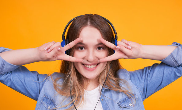 Young girl with headphones looks staright and holds peace near her face