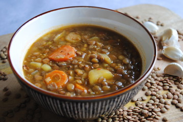 Vegan Lentil Soup with Vegetables served in brown bowl, on wooden kitchen board. Close up view.
