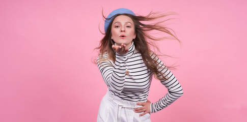 Young cute caucasian lady with flying hair in a fashionable beret on a pink background.