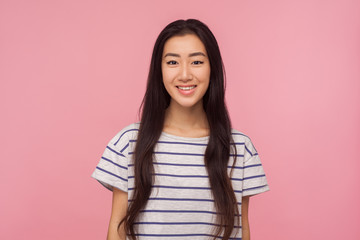 Portrait of cheerful pretty asian girl with long brunette hair in striped t-shirt looking at camera with toothy smile, enjoying happy life, good mood. indoor studio shot isolated on pink background