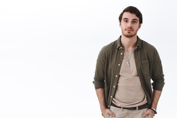 Portrait of handsome caucasian bearded male in stylish outfit, holding hands in pokets in cool pose standing white background, looking camera with slight smile, ready to go but waiting girlfriend